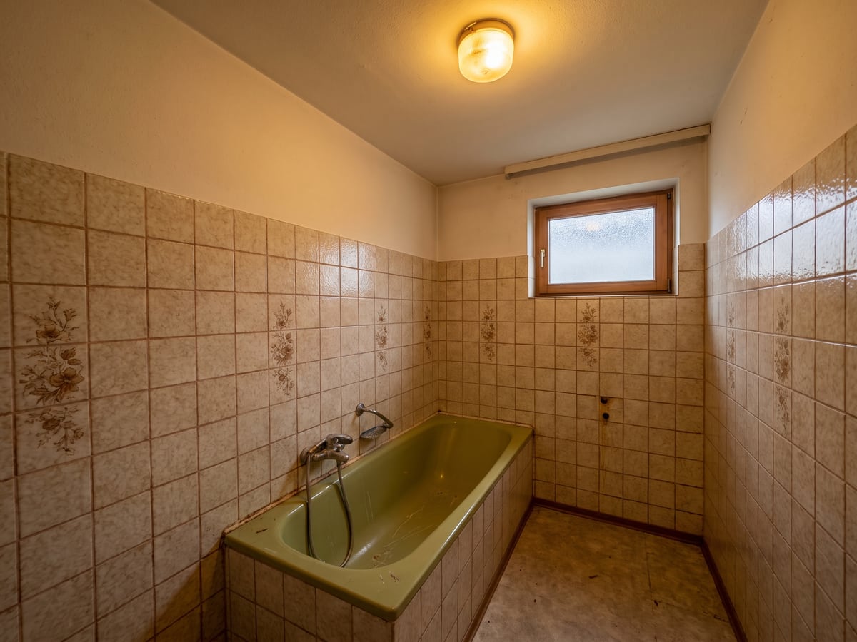 Badezimmer vor der Sanierung: gefliestes Bad im Zustand der 1980er Jahre mit alter Wanne